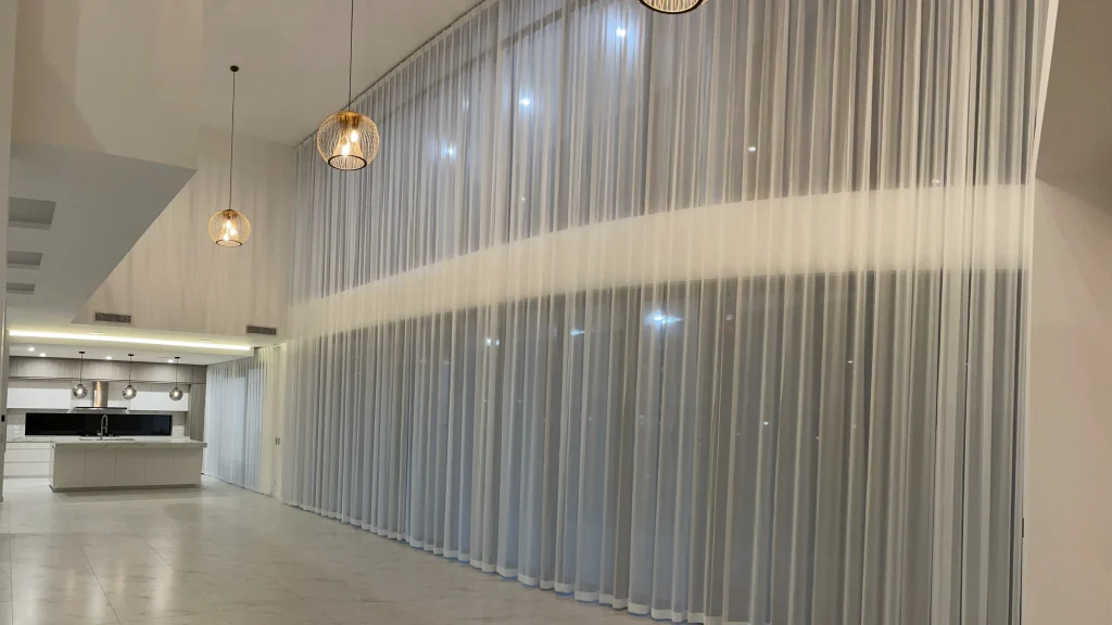 Pinch fold transparent sheers elegantly installed on a high and wide living room window